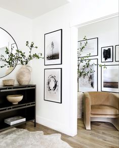 a living room with white walls and pictures on the wall next to a black dresser