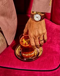 a man holding onto a glass with a drink in it on top of a pink chair