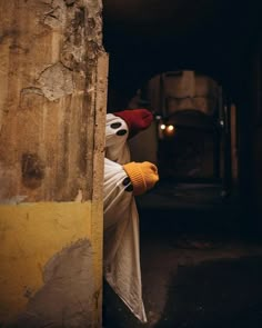 a person dressed as a ghost peeking out from behind a wall in an alleyway