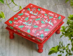 a small red table with birds painted on it and green leaves around the edges, sitting on a tile floor