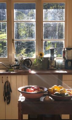 two bowls of fruit on a kitchen counter with sun shining through the window behind them