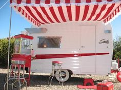 a red and white striped awning next to a parked camper on gravel ground