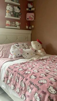 two hello kitty stuffed animals sitting on top of a pink bedspread in a bedroom