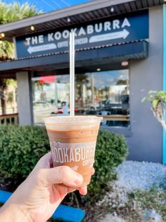 a hand holding up a drink in front of a building with the kokabuki logo on it