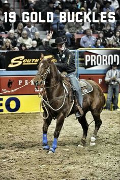 a man riding on the back of a brown horse in front of an arena filled with people