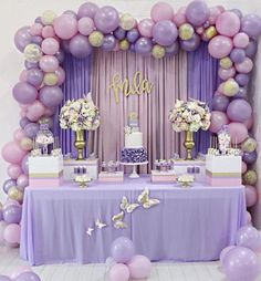 a table topped with lots of purple and white balloons next to a cake on top of a table