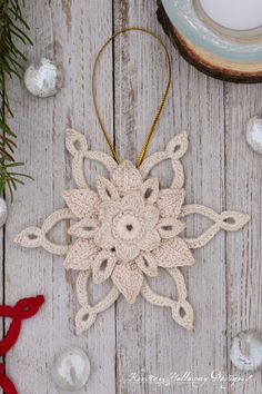 a crocheted snowflake ornament hanging on a wooden table with ornaments around it