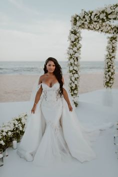 a woman in a wedding dress standing on the beach with flowers and candles around her