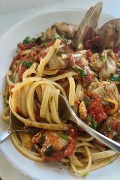 a white plate topped with pasta covered in sauce and meat next to clams on top of a wooden table