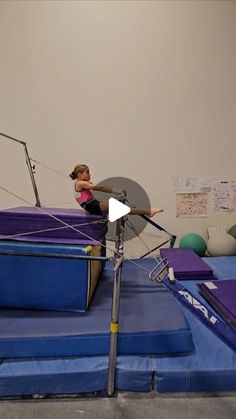 a girl is on a trampoline in an indoor area with purple mats and ropes