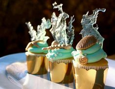 three cupcakes with frosting and sea shells on them sitting on a plate