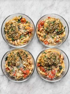 four clear bowls filled with different types of pasta and sauce on top of a marble table