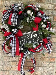 a christmas wreath hanging on the side of a brick wall with red and black ribbon