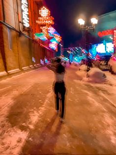 a woman standing on the side of a road in front of neon signs and buildings