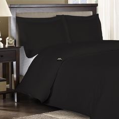 a bed with black sheets and pillows in a room next to a night stand on a rug