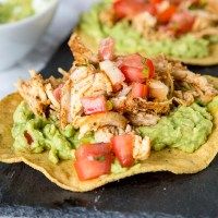 two tortilla shells topped with chicken, tomatoes and avocado on a black tray