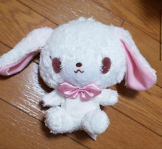 a white stuffed animal with a pink bow on it's head sitting on a wooden floor