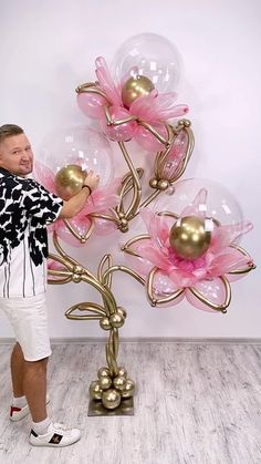 a man standing in front of a large balloon tree with pink flowers on it's branches