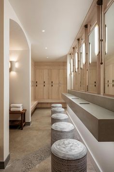 a long bathroom with multiple sinks and mirrors on the wall, along with several stools