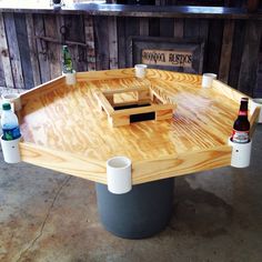 a wooden table with two cups and bottles on the top, in front of a bar