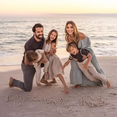 a family poses on the beach at sunset with their child's name written in the sand