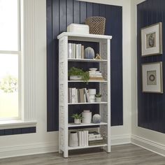 a white book shelf with books and plants on it in a room painted navy blue