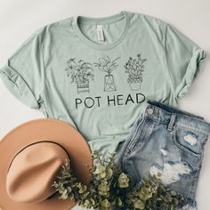 Pot Head T-Shirt - a funny, eye-catching shirt with boho potted plant designs. This cute graphic tee is perfect for the plant lover or gardener with a green thumb. Our T-shirt feels soft and light with just the right amount of stretch. It's pre-shrunk, comfortable and flattering for both men and women. Please note that although the size options in the dropdown box say 'Men's', this is a unisex T-shirt. Refer to the size chart in the photos for measurements. Solid colors are 100% combed and ring-spun cotton. Heather colors are 52% combed and ring-spun cotton and 48% polyester. Heather prism colors are 99% combed and ring-spun cotton and 1% polyester. Care Instructions: Machine wash cold, inside-out, gentle cycle with mild detergent and similar colors. Use non-chlorine bleach, only when nece Graphic Tee Crew Neck T-shirt, Spring Relaxed Fit T-shirt With Plant Details, Relaxed Fit Graphic Print Shirt For Gardening, Relaxed Fit Shirt With Graphic Print For Gardening, Casual Summer Tops With Plant Details, Casual Relaxed Fit T-shirt With Plants, Green T-shirt With Plants Print, Relaxed Fit, Green Relaxed Fit T-shirt With Plant Detail, Crew Neck Cotton T-shirt With Plant Details