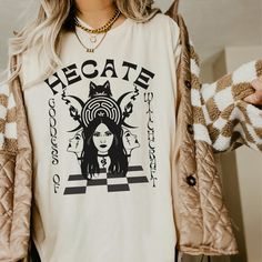 Get ready to be OBSESSED with your new Hecate Goddess Greek Mythology shirt. It's the cutest and most trendy way to combine all those important trendy light academia and greek apparel vibes! This is the perfect mythology shirt!  * Q U I C K * F A C T S * ✺  All shirts are UNISEX ✺  100%  ringspun cotton (fiber content may vary for different colors) ✺  Soft-washed, garment-dyed fabric brings extra coziness ✺  Wash and dry normally (on cool for best results) ✺  Sewn-in twill label * S I Z I N G * ✺ For an oversized fit, select two or three sizes up from your normal size ✺ Model is wearing size L  ✺ Sizing runs true to size ✺ Relaxed fit ✺ Most women find their typical size works best, since they are meant to fit a touch loose ✺ See Size guide and fit in images          * S H I P P I N G * T Goddess Greek, Goddess Hecate, Snake Shirt, Hecate Goddess, Greek Apparel, Triple Goddess, Greek Clothing, Light Academia, Greek Goddess