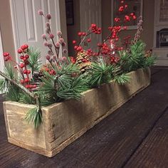 a wooden planter filled with red berries and greenery on top of a table