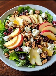 a salad with apples, cranberries, walnuts and feta cheese in a white bowl