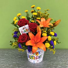 a birthday bouquet with orange lilies, red roses and yellow daisies in a bucket