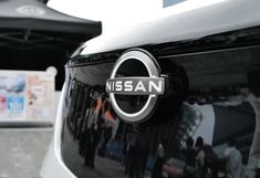 the nissan logo is shown on the front of a white and black car with people walking by