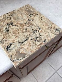 a marble counter top in a kitchen with white tile flooring and brown cabinet doors