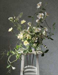 a white chair with flowers in it and greenery on the back side, against a gray wall