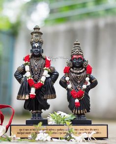 two black statues with red and white garlands on their heads sitting next to each other