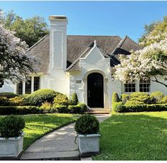 a white house with bushes and trees in the front yard on a sunny day,