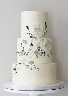 a three tiered cake with white flowers and leaves on the top is sitting on a shelf