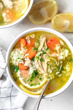 two bowls filled with chicken and rice soup next to sliced lemons on the side