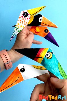 four colorful birds are being held up by someone's hand on a blue background