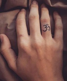 a person's hand with a small tattoo on the middle finger and an om symbol in the middle