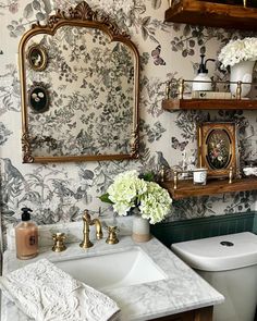 a white toilet sitting next to a bathroom sink under a mirror above a wooden shelf