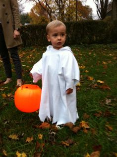 a little boy dressed as a ghost holding an orange ball