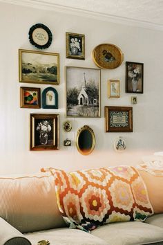 a living room filled with lots of pictures and framed objects on the wall next to a couch