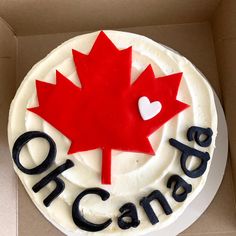 a white cake with red and black frosting that says canada on the side, in front of a cardboard box