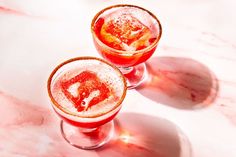 two glasses filled with liquid sitting on top of a marble counter topped with ice and sprinkles