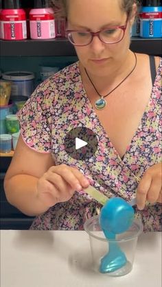 a woman is pouring something into a glass with a blue object in the foreground