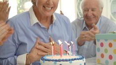 an older couple celebrating their birthday with cake and hands in the air, while another man claps his hand