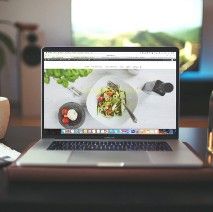 an open laptop computer sitting on top of a wooden desk next to a cup of coffee