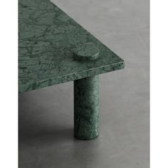 a green marbled table with a round knob on it's end, sitting on a gray floor