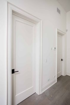 an empty room with two white doors and wood flooring on either side of the door